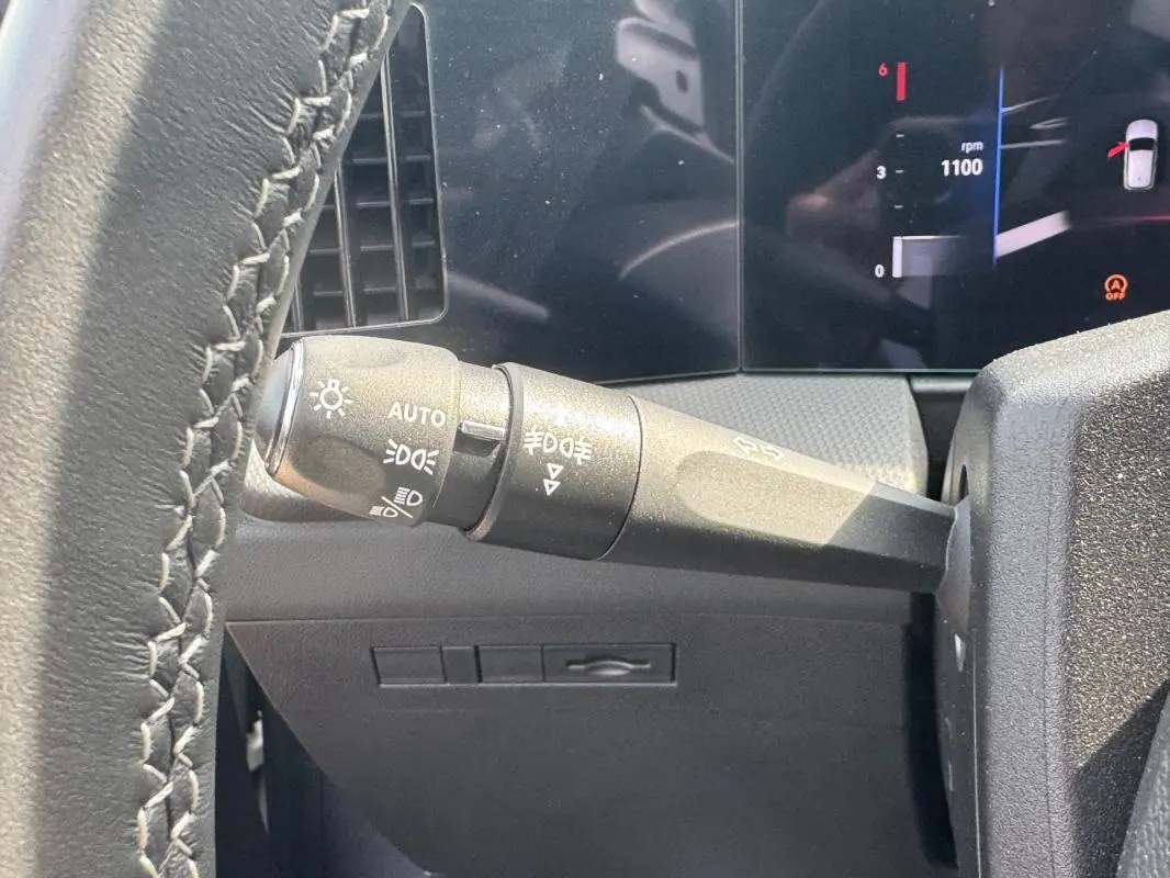 Gros plan sur le commodo d’éclairage à gauche du volant cuir de l’Opel Astra gris 2024, tableau de bord numérique visible.