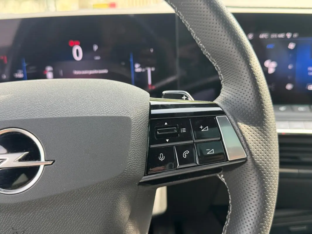 Gros plan sur le volant cuir perforé gris de l’Opel Astra 2024 avec commandes intégrées et tableau de bord numérique flou.