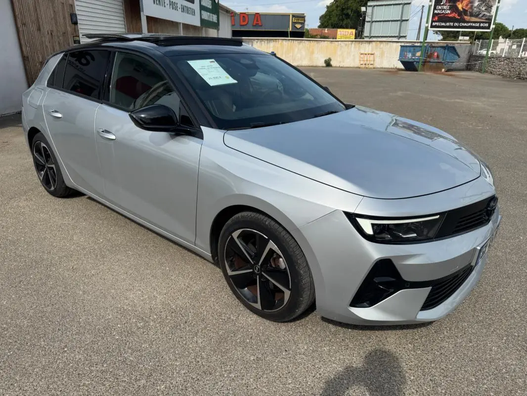 Vue 3/4 avant droite d'une Opel Astra gris clair avec jantes alliage noires et vitres surteintées.
