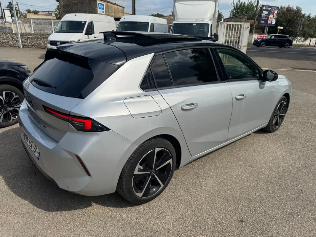 Opel Astra gris clair vue 3/4 arrière droit avec toit noir, jantes alliage 17 pouces et vitres surteintées.