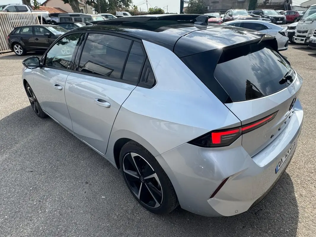 Opel Astra gris 3/4 arrière droit avec toit noir, vitres surteintées et jantes alliage 17 pouces.