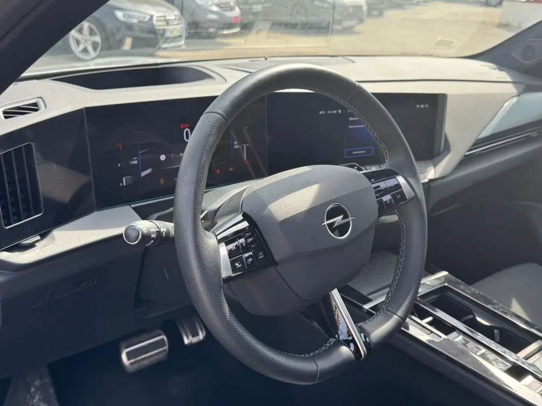 Vue intérieure centrée sur le volant cuir noir de l'Opel Astra 2024, avec tableau de bord numérique et console moderne.