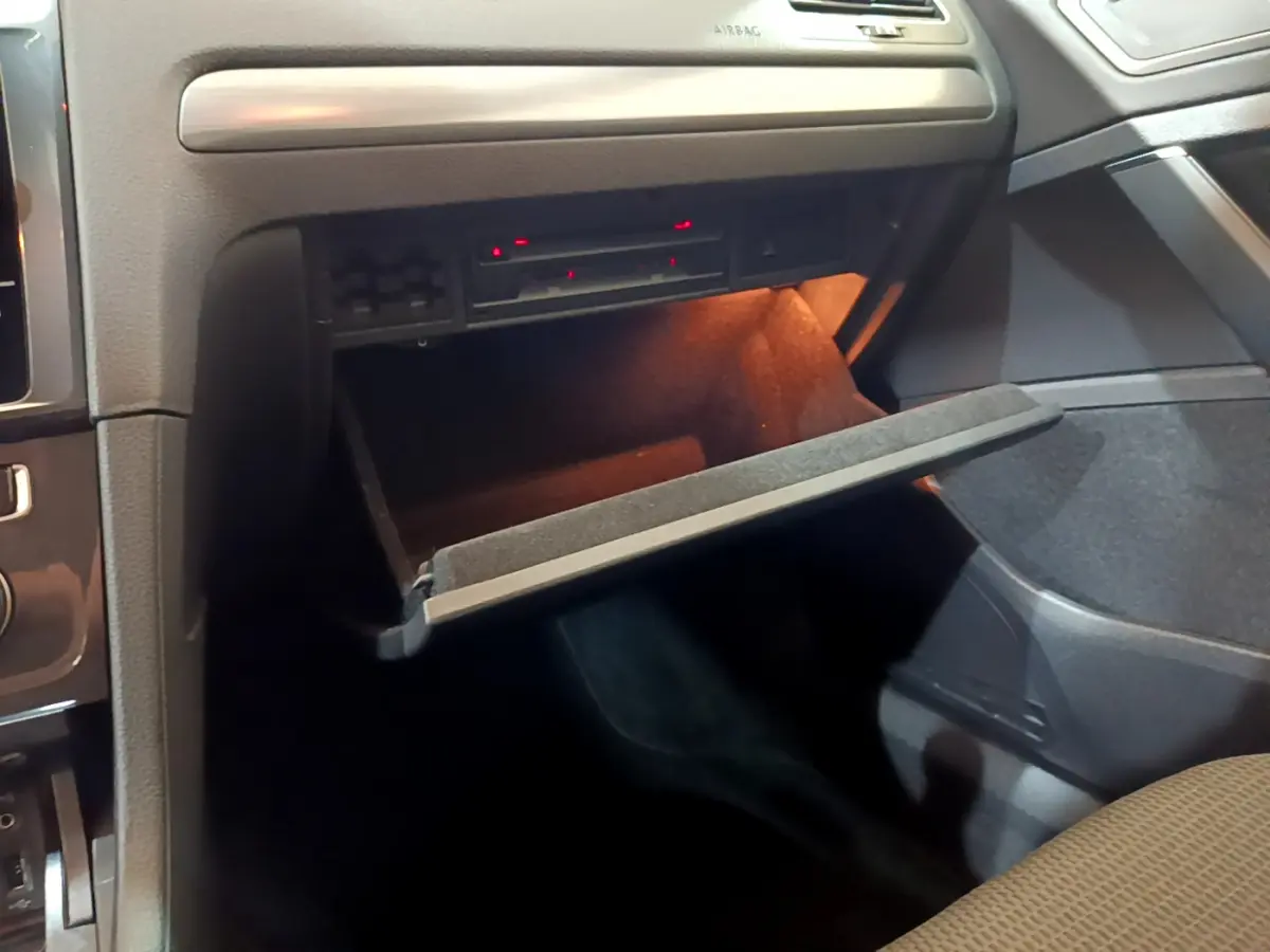 Gros plan sur la boîte à gants ouverte avec éclairage intérieur dans l'habitacle noir de la Volkswagen Golf 2018.