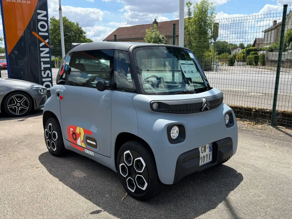Vue 3/4 avant droite d'une Citroën Ami MY AMI POP 2024 gris clair avec stickers colorés et phares LED carrés.