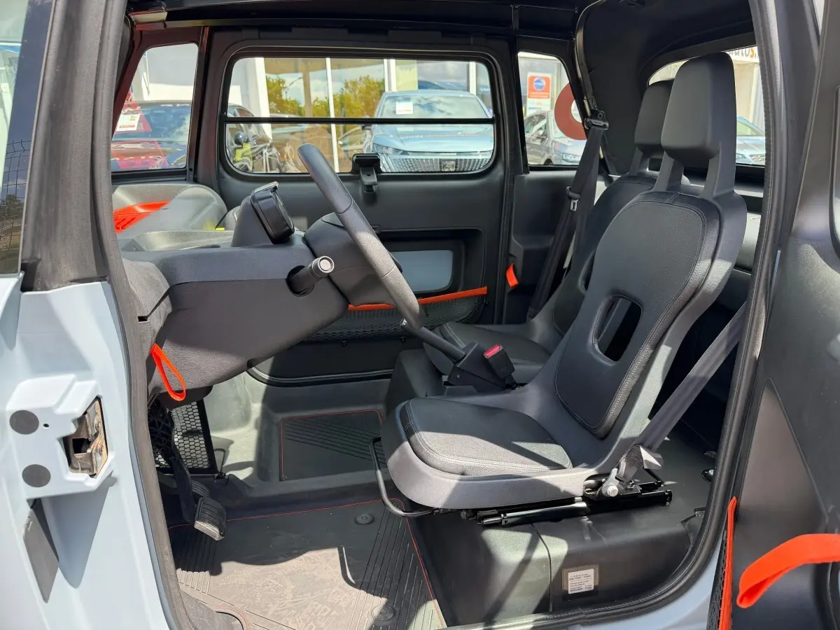 Intérieur côté conducteur du Citroën Ami MY AMI POP 2024, sièges noirs et détails orange, volant et tableau de bord minimalistes.
