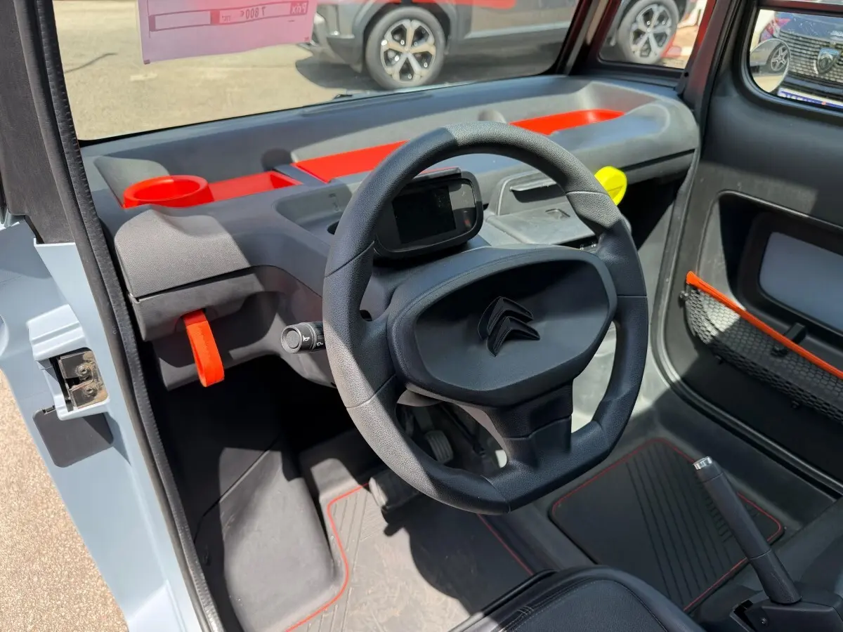 Vue intérieure côté conducteur du tableau de bord noir et gris avec touches orange vif de la Citroën Ami MY AMI POP 2024.