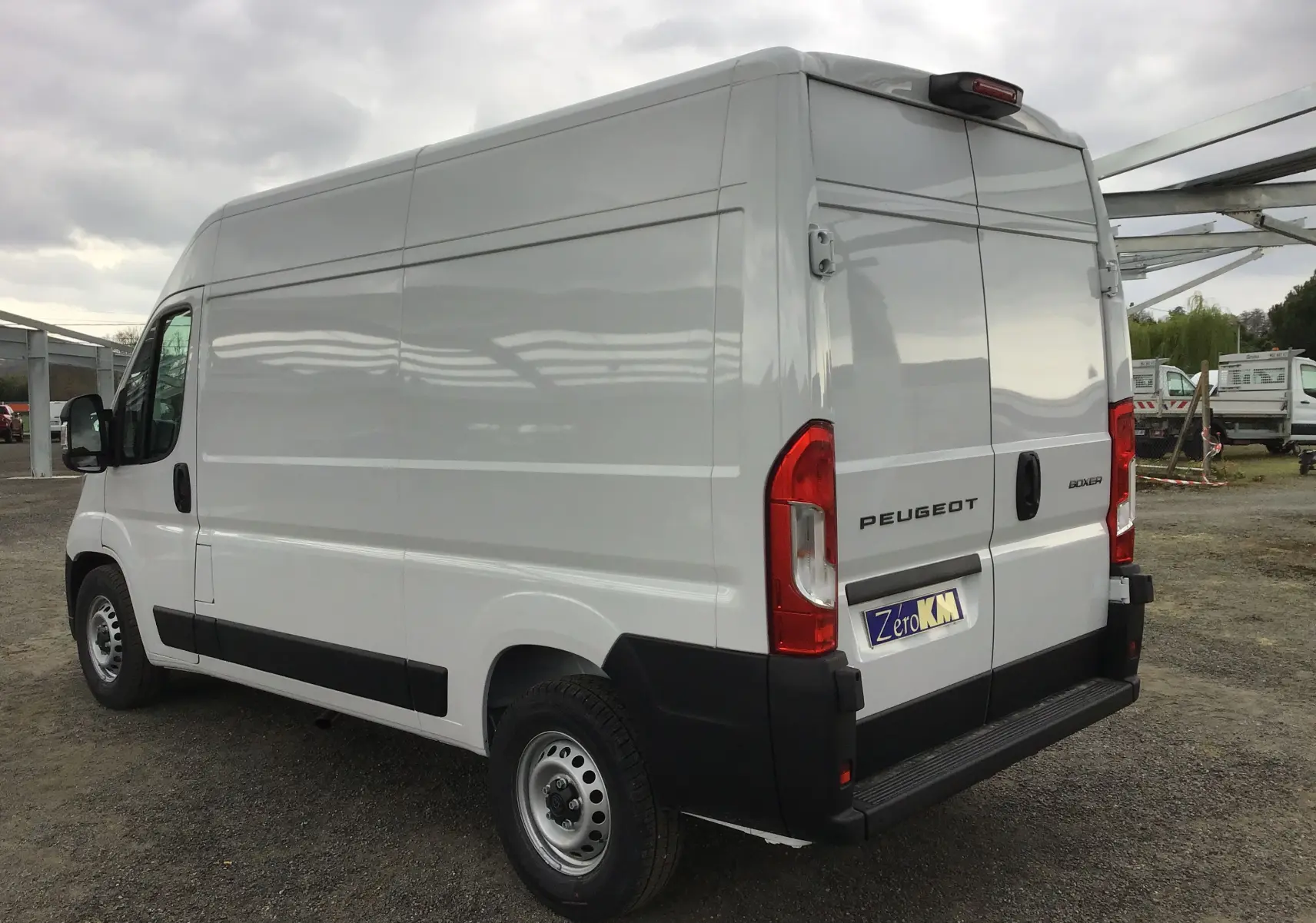 Vue 3/4 arrière gauche d'un Peugeot Boxer Fourgon blanc 2025 avec portes arrière fermées sur un parking extérieur.
