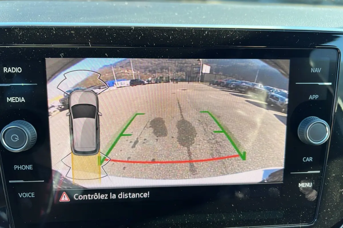 Vue de la caméra de recul du Volkswagen T-Cross blanc pur, affichant les lignes de guidage et l'alerte de distance.