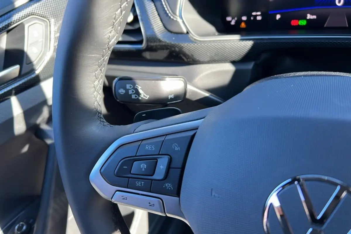 Gros plan sur le volant cuir multifonctions côté gauche du Volkswagen T-Cross blanc avec commandes de régulateur adaptatif.