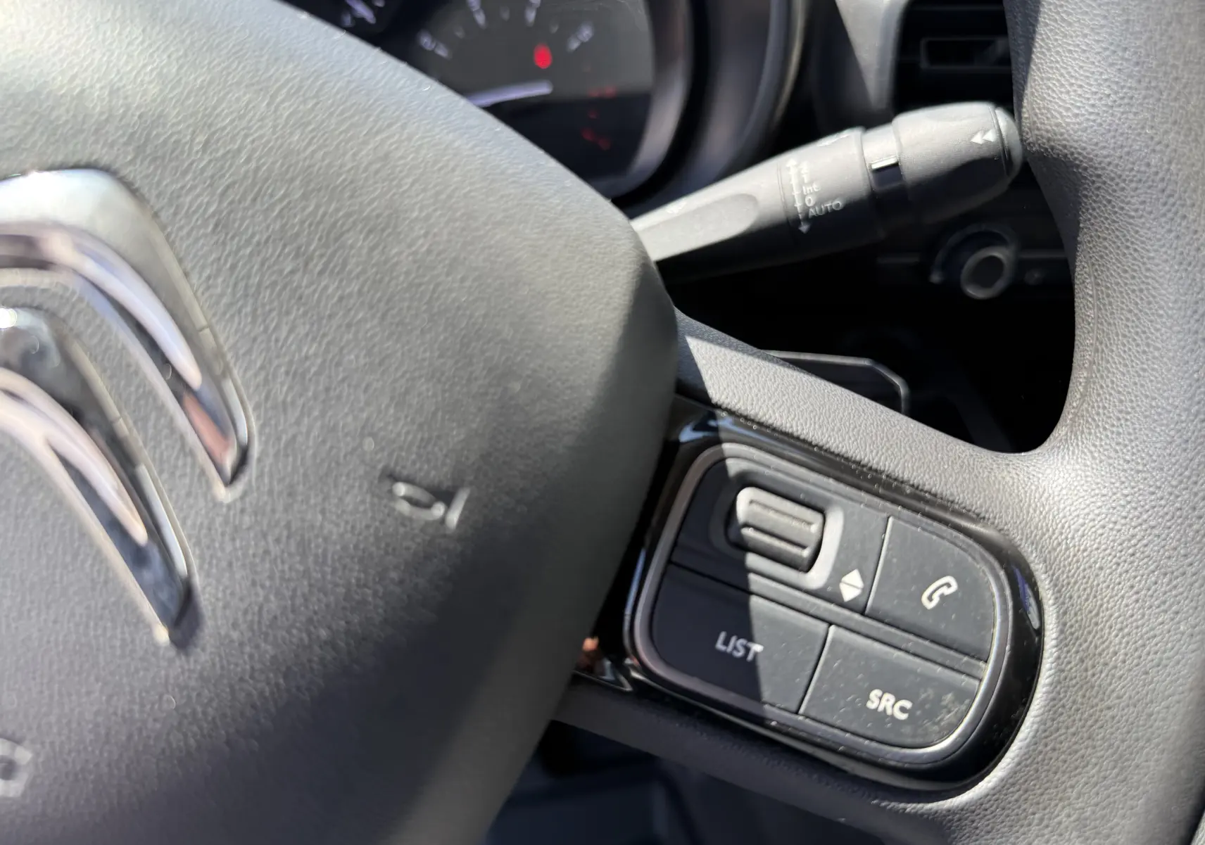 Gros plan sur le volant noir du Citroën Berlingo XL 2022 avec commandes intégrées et tableau de bord en arrière-plan.