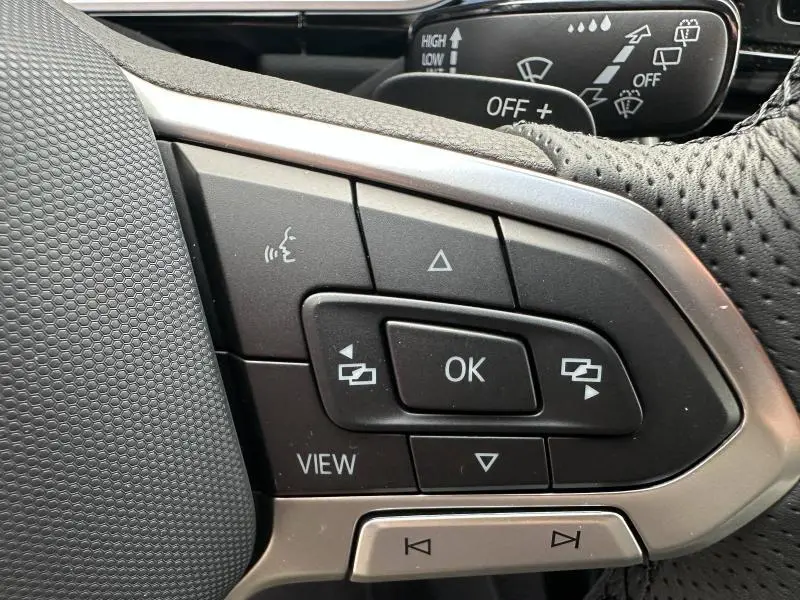 Gros plan sur les commandes au volant du Volkswagen T-Roc 2025, finition R-Line, avec cuir perforé noir et boutons multifonctions.