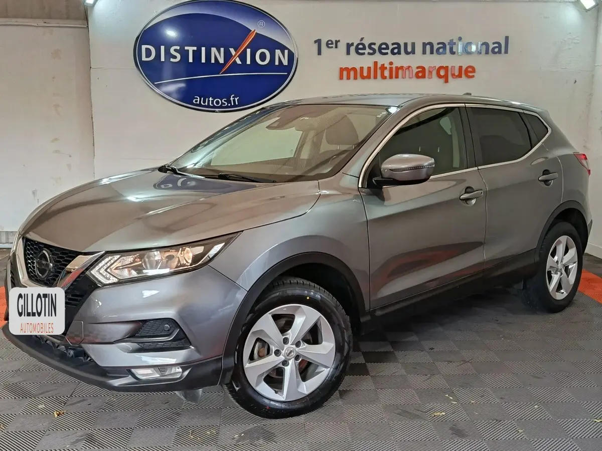 Nissan Qashqai gris clair 2019 en 3/4 avant droit, avec jantes alliage et phares allumés dans un showroom.