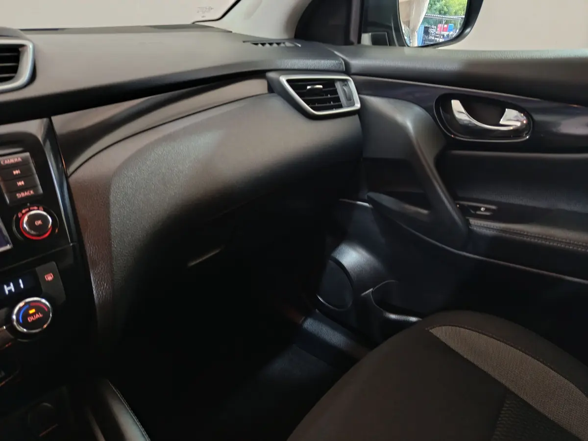 Intérieur côté passager du Nissan Qashqai gris clair, tableau de bord noir avec aérateurs et porte en cuir noir.