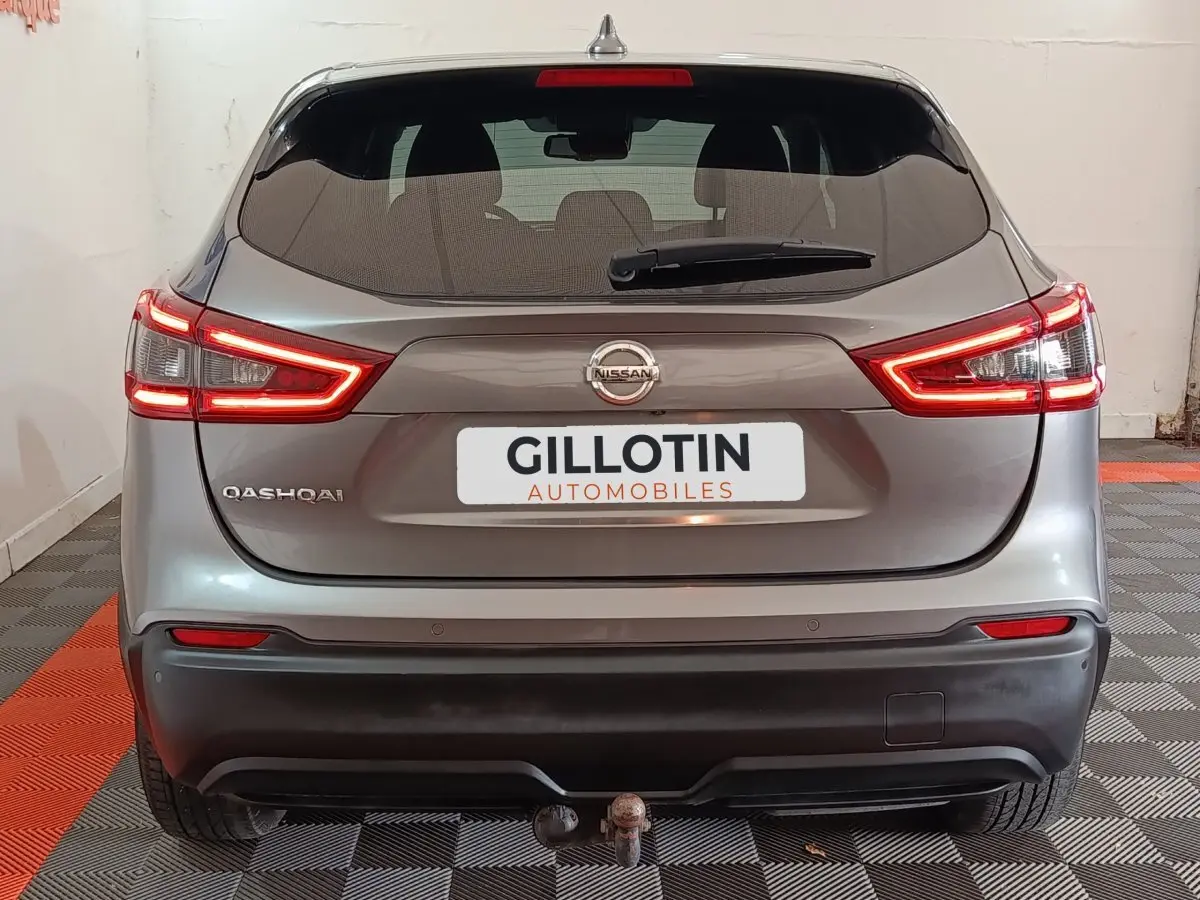Vue arrière d'un Nissan Qashqai gris clair avec feux LED allumés et attelage visible en intérieur showroom.
