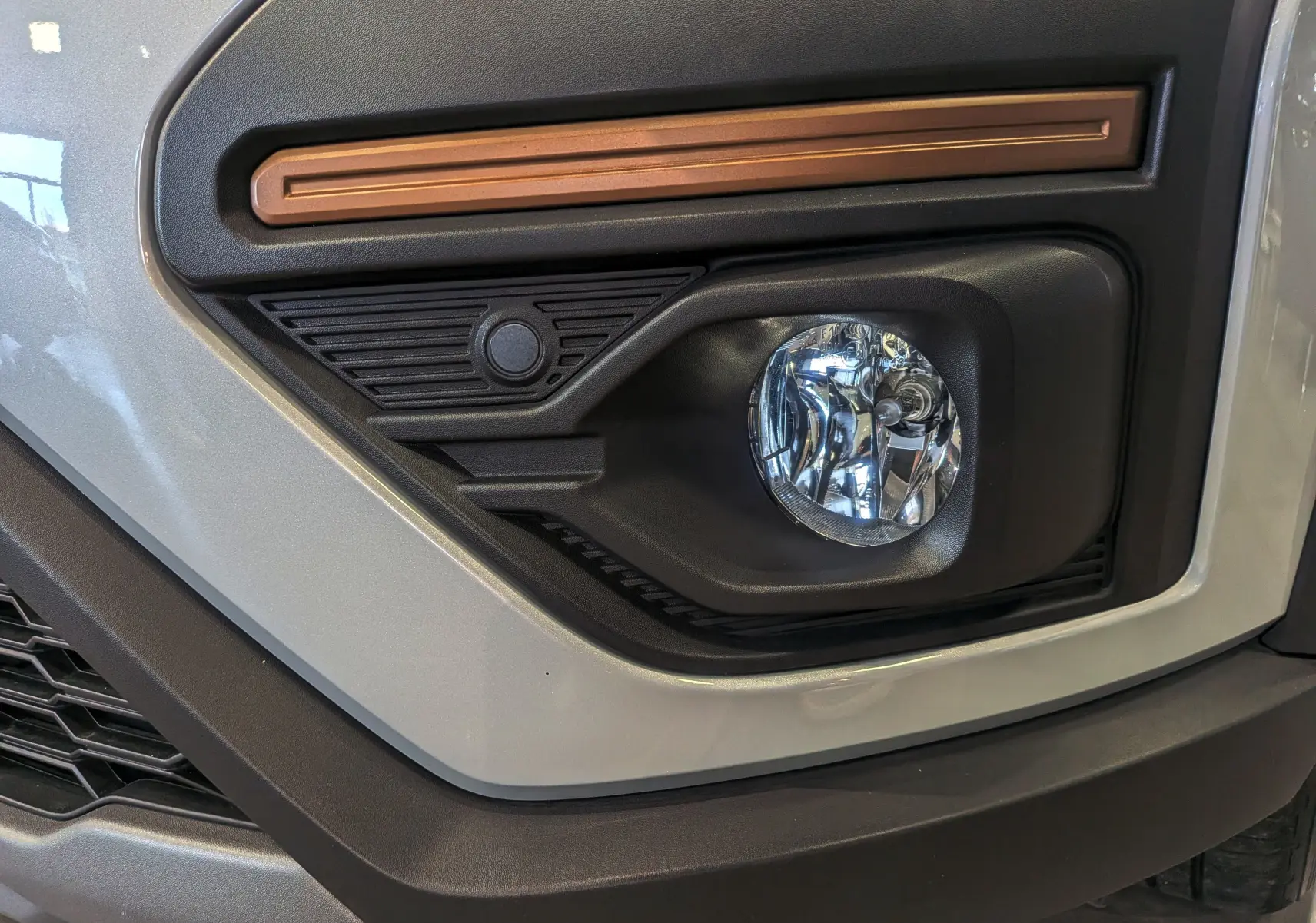 Gros plan sur le feu antibrouillard avant droit d'une Dacia Sandero Stepway gris Moonstone avec détails noirs et orange.