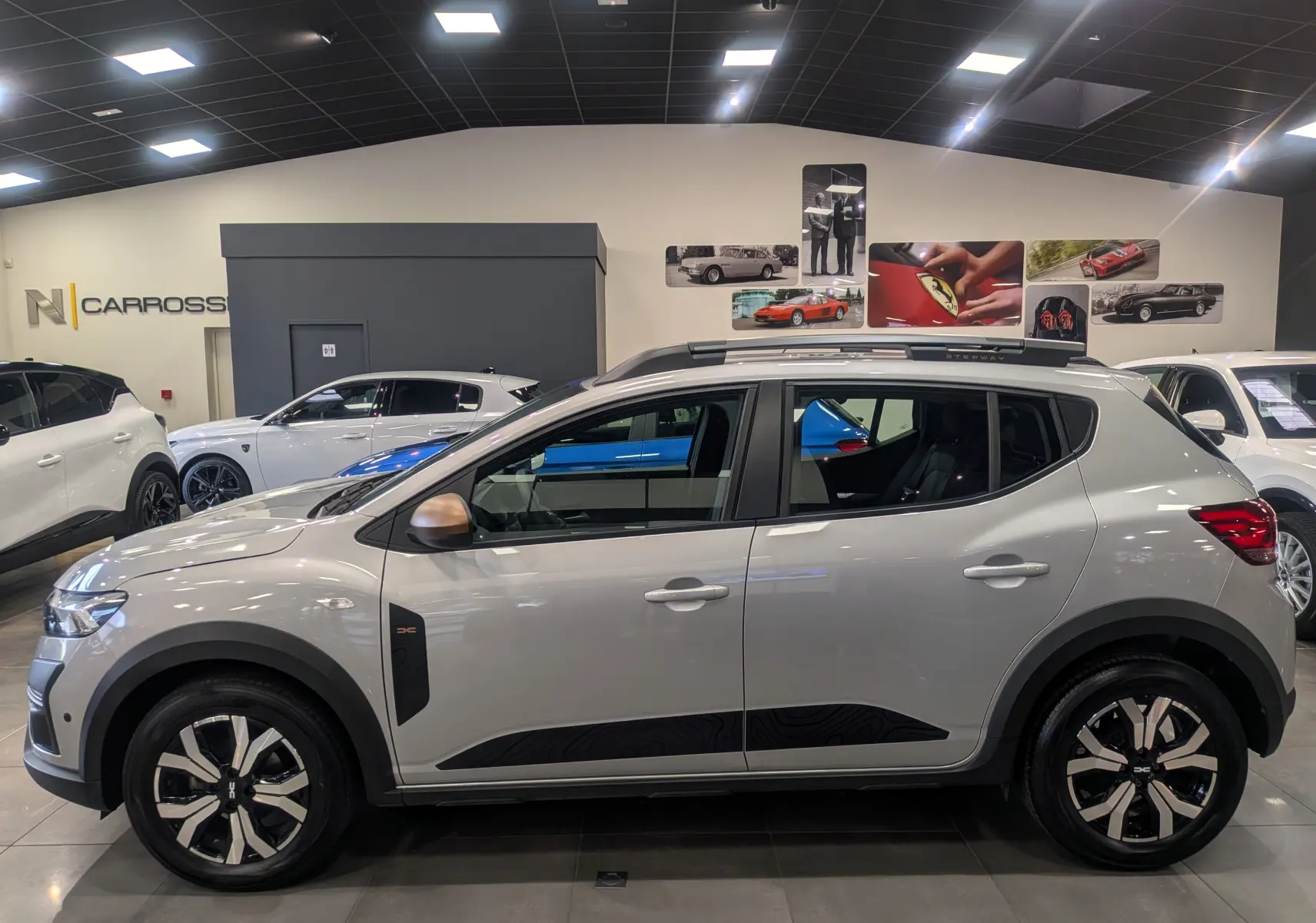 Vue de profil droit d'une Dacia Sandero Stepway 2023 gris Moonstone avec jantes bi-ton et barres de toit noires.
