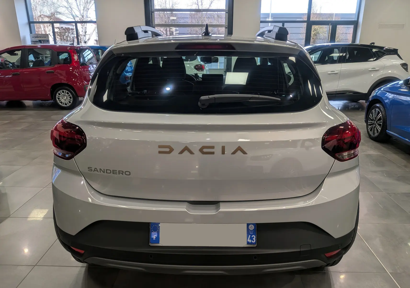 Vue arrière d'une Dacia Sandero Stepway gris Moonstone en showroom, avec logo et feux arrière visibles.