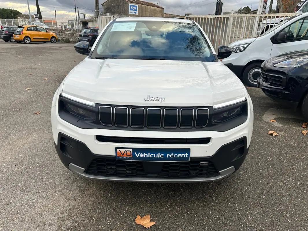 Vue de face d’un Jeep Avenger blanc 2024 avec calandre noire et phares LED intégrés, sur parking extérieur.