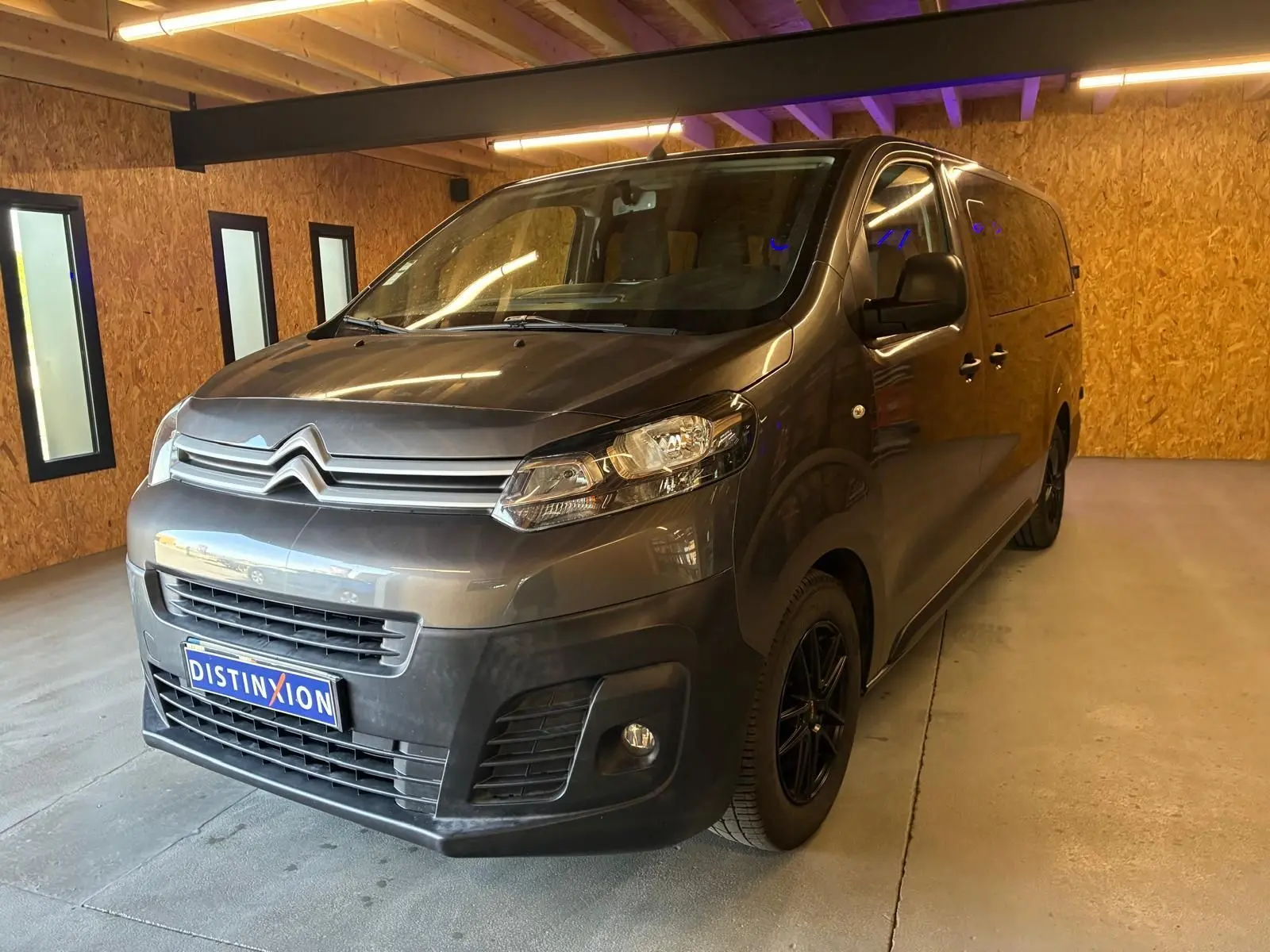 Vue 3/4 avant droit d'un Citroën Jumpy XL Spacetourer gris, avec calandre chromée et jantes noires, en intérieur.