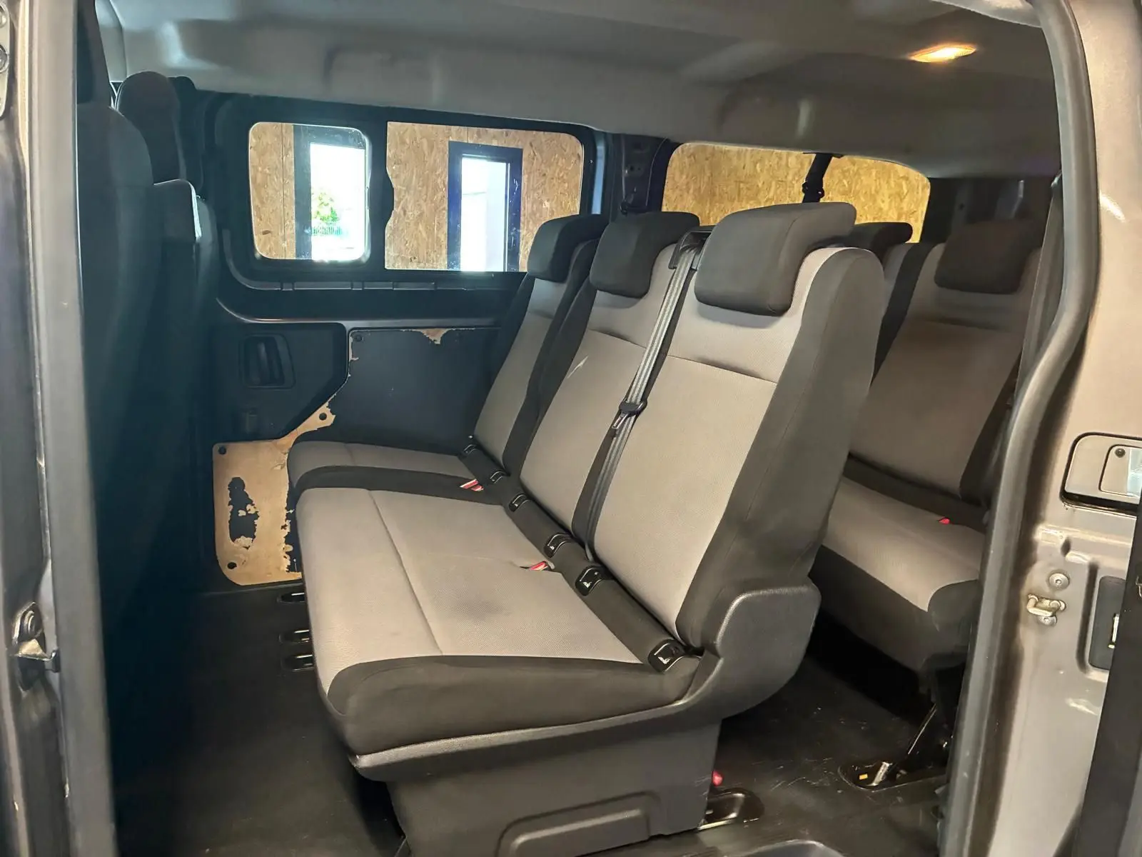 Vue intérieure côté droit du Citroën Jumpy XL Spacetourer gris, montrant les sièges tissu 9 places et la porte coulissante ouverte.