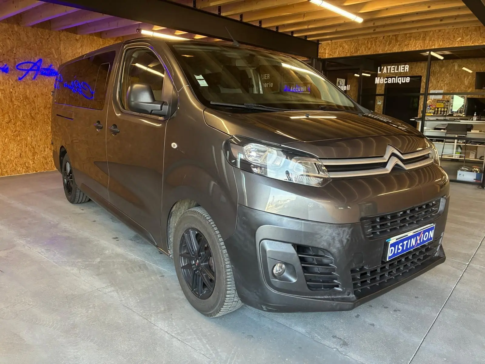 Vue 3/4 avant droit d'un Citroën Jumpy XL Spacetourer gris, avec jantes noires et calandre marquée, en intérieur d'atelier.