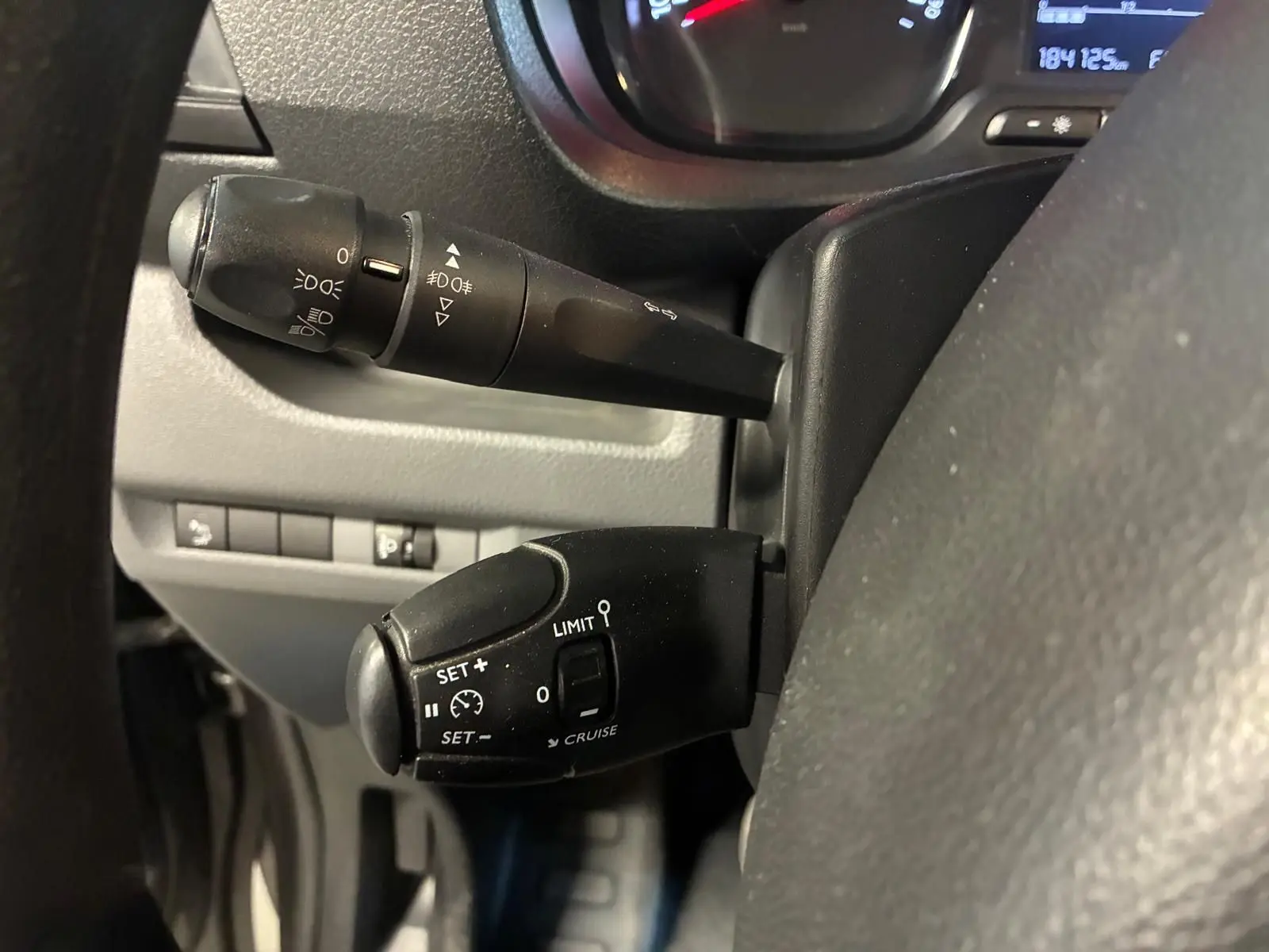 Gros plan sur les commandes de régulateur de vitesse et feux au volant d'un Citroën Jumpy gris, tableau de bord partiel visible.
