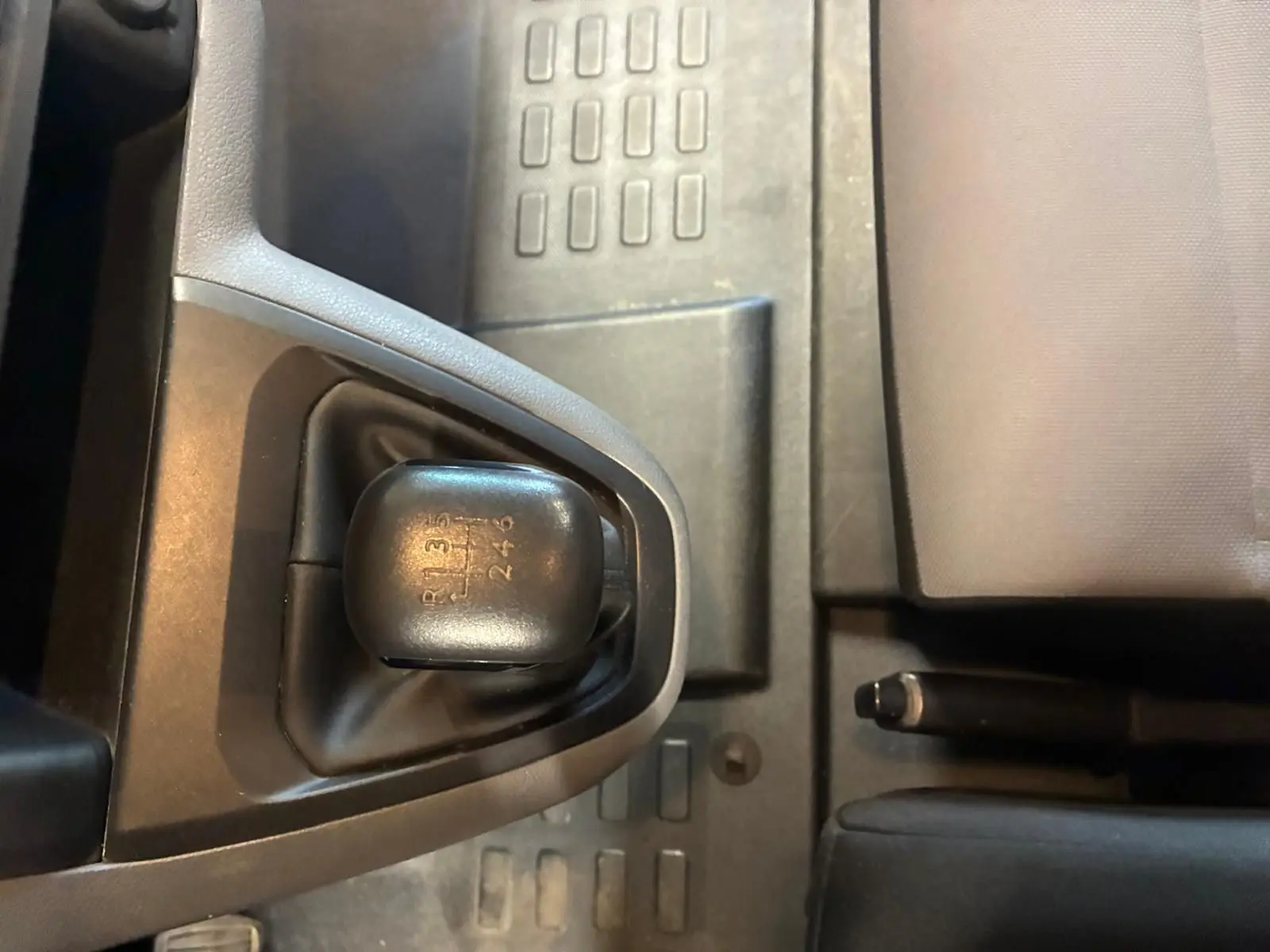 Gros plan sur le levier de vitesses manuel noir du Citroën Jumpy gris, avec frein à main et siège tissu visibles.