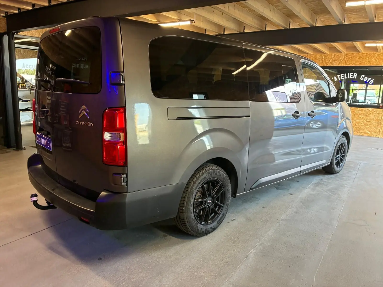 Vue 3/4 arrière droite d’un Citroën Jumpy XL Spacetourer gris avec vitres teintées et jantes noires en intérieur d’atelier.