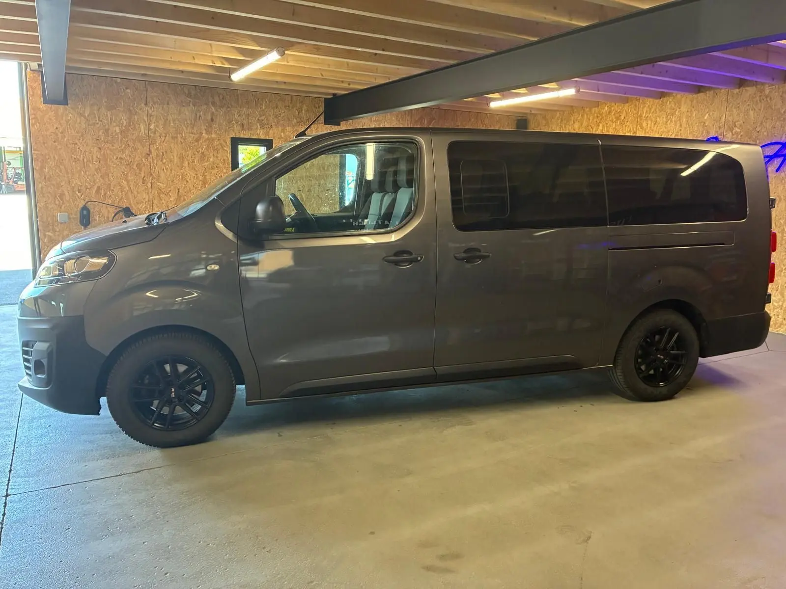 Vue de profil côté gauche d’un Citroën Jumpy XL Spacetourer gris avec vitres arrière teintées et jantes noires.