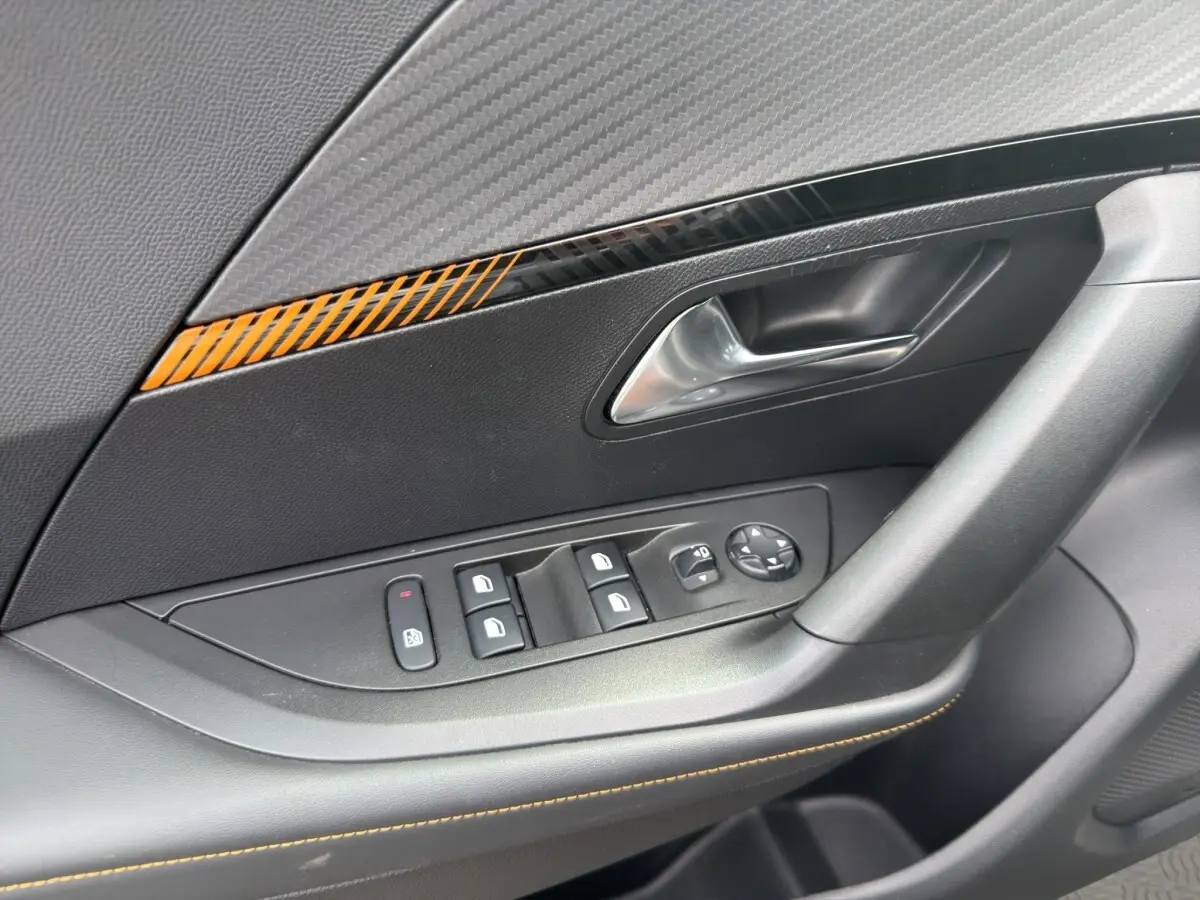 Gros plan sur la porte côté conducteur du Peugeot 2008 gris foncé, avec commandes des vitres et insert décoratif orange.