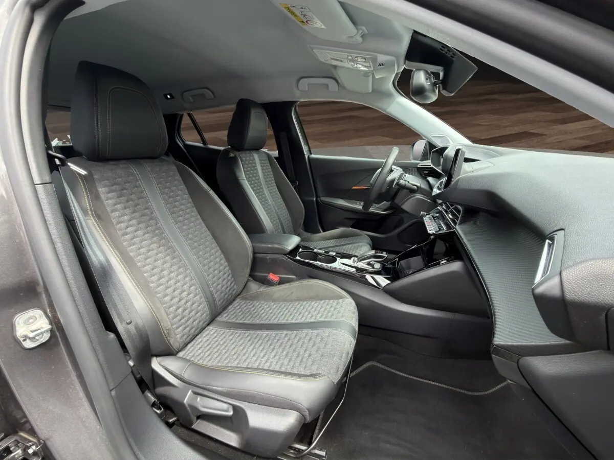 Vue intérieure côté gauche du Peugeot 2008 gris foncé, montrant les sièges avant en tissu et cuir avec surpiqûres contrastées.