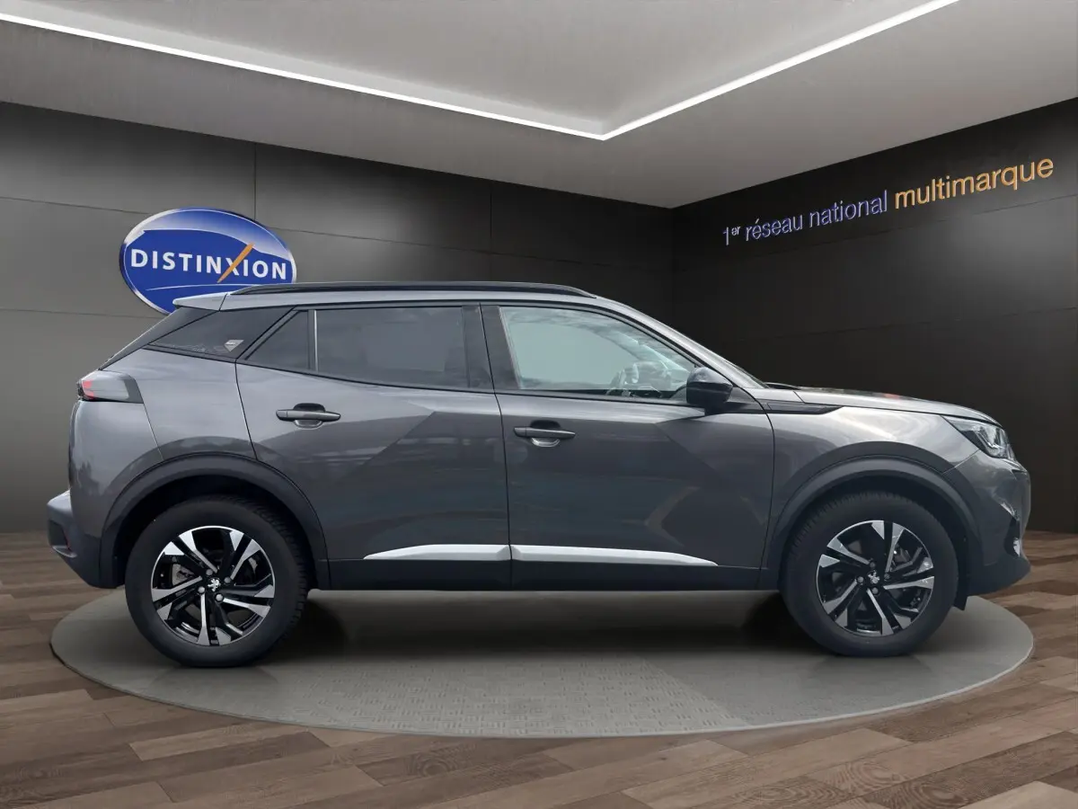 Profil côté droit d'un Peugeot 2008 gris foncé 2022 avec jantes alliage et toit noir en showroom.