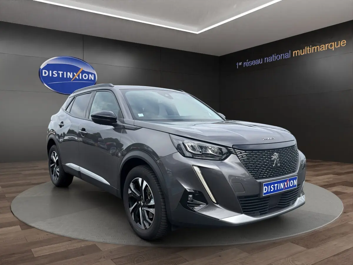 Peugeot 2008 gris foncé en 3/4 avant droit, avec calandre noire et feux LED distinctifs, sur podium intérieur.
