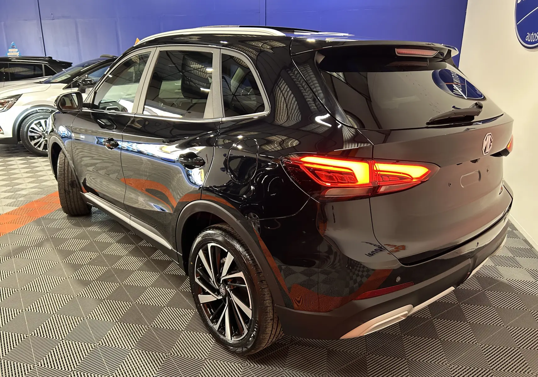 Vue 3/4 arrière droite du MG ZS Hybrid+ 197 Luxury noir Pebble avec feux arrière allumés et toit panoramique ouvrant.