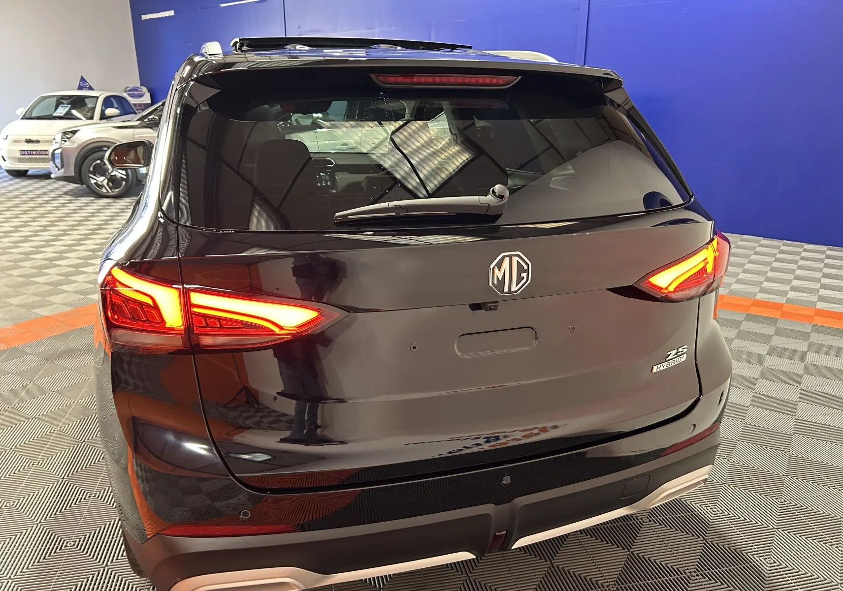 Vue arrière d’un MG MOTOR ZS Hybrid+ 197 Luxury noir Pebble avec feux LED allumés et toit panoramique ouvrant visible.
