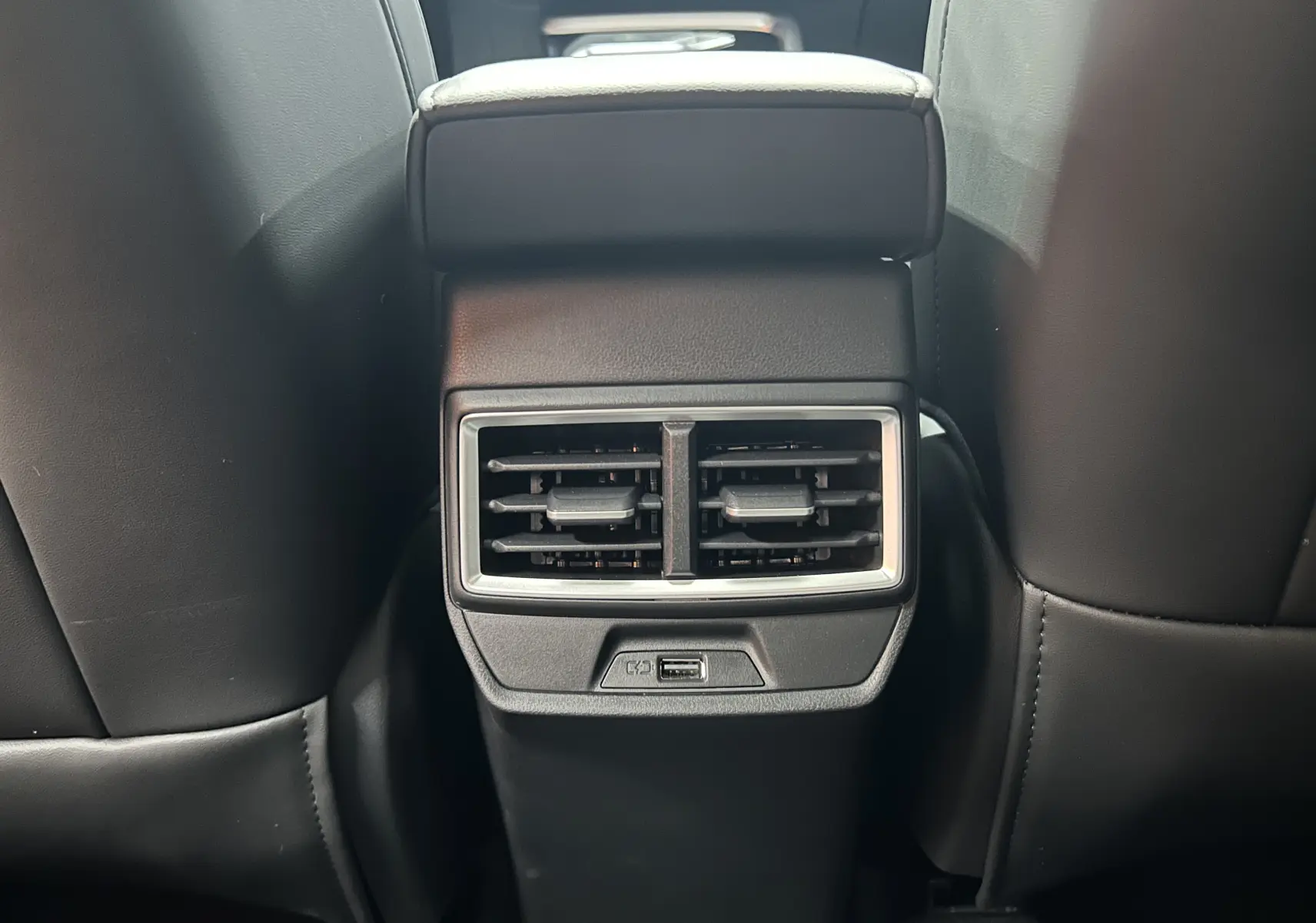 Vue rapprochée des aérateurs arrière et port USB intégrés entre les sièges avant en cuir noir du MG MOTOR ZS Hybrid+ 2026.