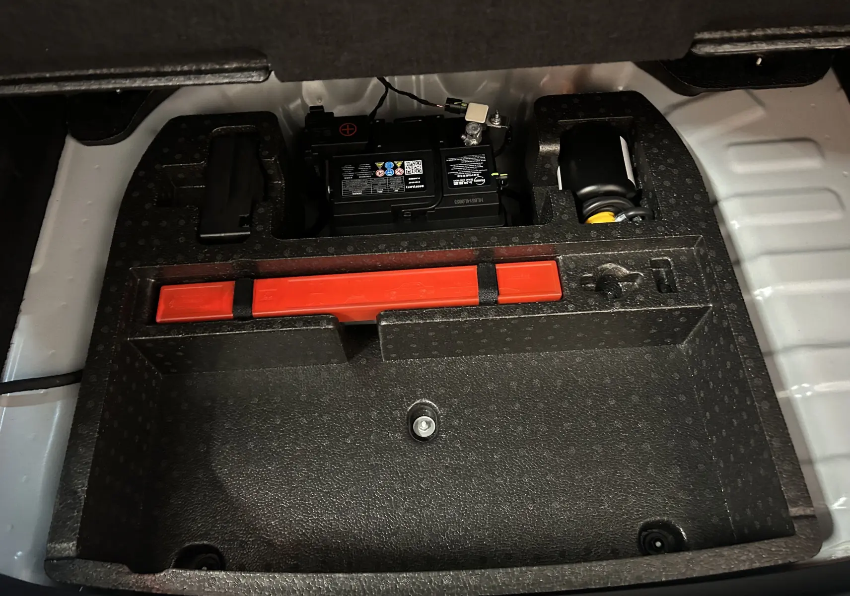Vue rapprochée du compartiment batterie et kit de secours dans le coffre du MG Motor ZS Hybrid+ 197 Luxury Pebble Black.