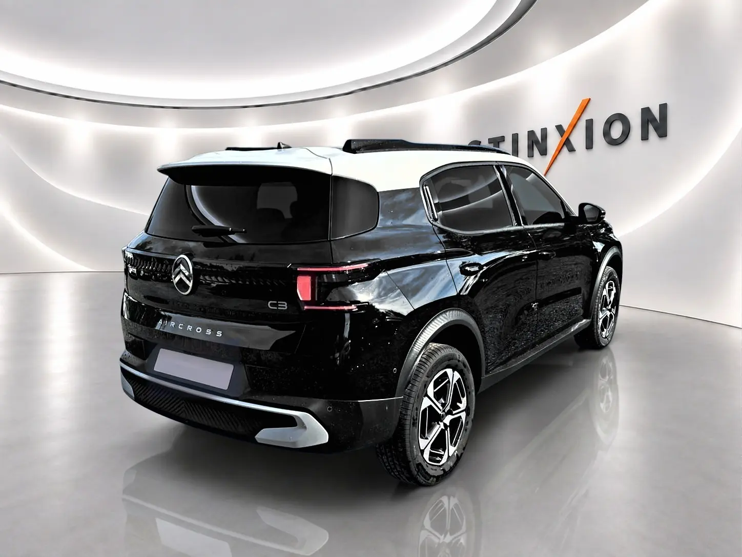Vue 3/4 arrière droite d'une Citroën C3 Aircross noire avec toit blanc et jantes alu distinctives dans un showroom lumineux.
