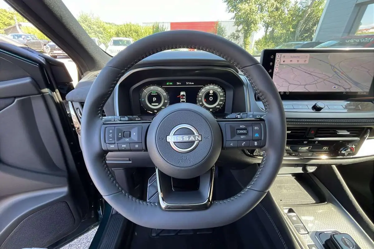 Vue intérieure centrée sur le volant cuir multifonctions du Nissan Qashqai E-POWER 205 N-DESIGN avec écran digital et navigation.