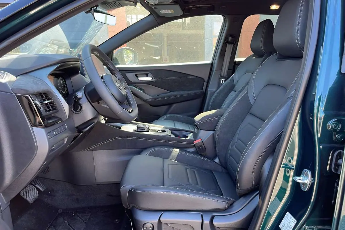 Vue intérieure côté conducteur du Nissan Qashqai E-POWER 205 N-DESIGN 2026, sièges cuir alcantara noirs et portière vert cayuga ouverte.