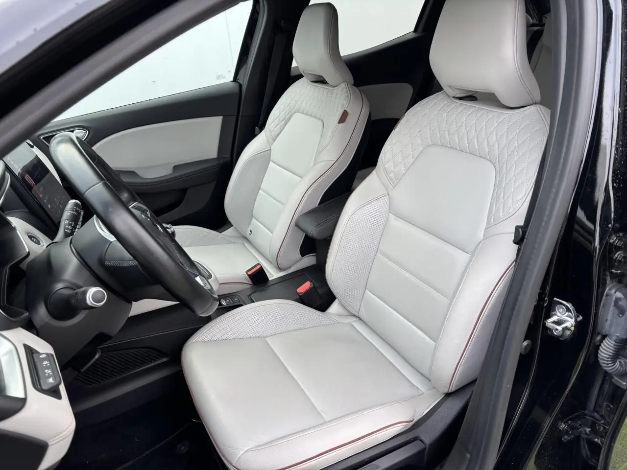 Intérieur de Renault Clio V 2020 vue côté conducteur, sièges cuir blanc avec surpiqûres et accoudoir coulissant noir.