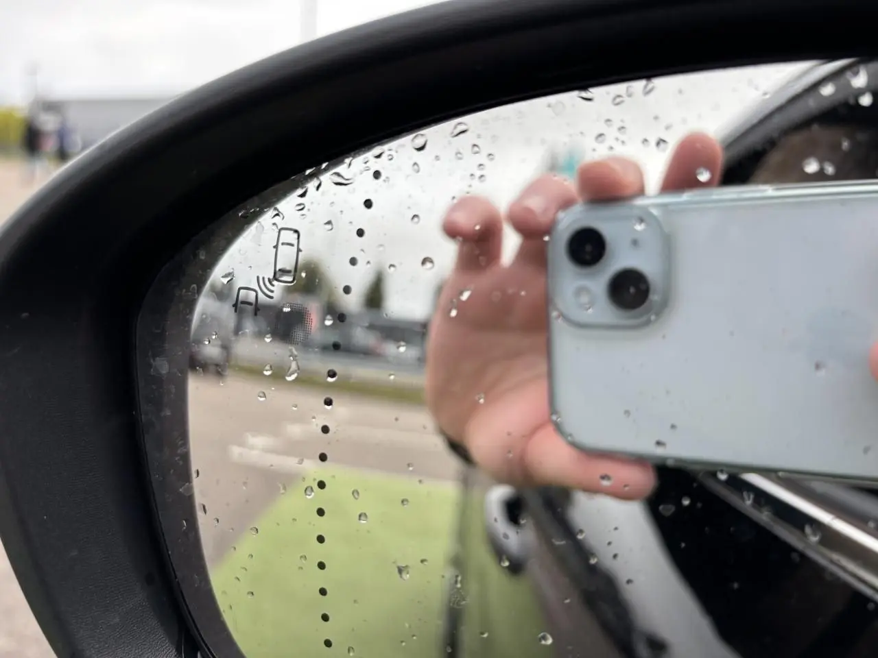 Reflet de la portière noire étoile d'une Renault Clio 2020 dans le rétroviseur côté gauche sous la pluie.