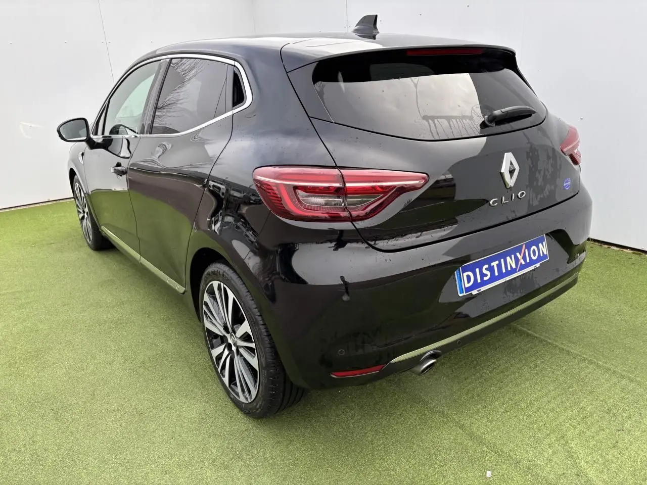 Vue 3/4 arrière gauche d'une Renault Clio noire étoile avec jantes alliage et échappement chromé sur sol vert.