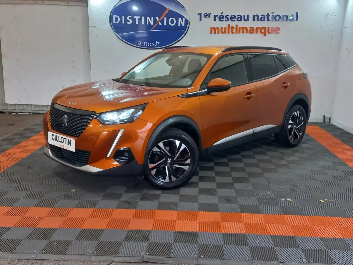 Peugeot 2008 orange en 3/4 avant droit, avec phares LED allumés et jantes noires à motifs argentés.