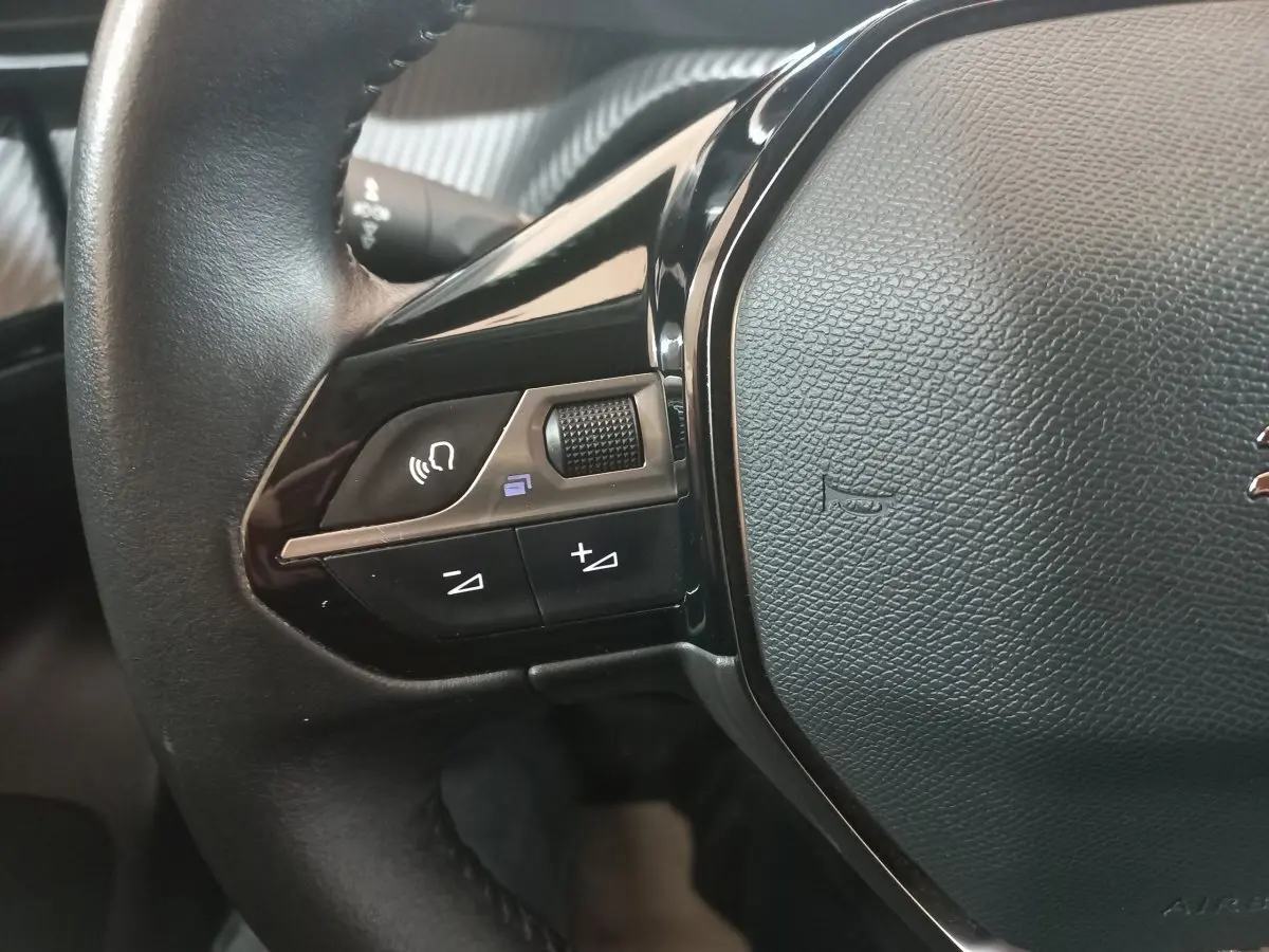 Gros plan sur la partie gauche du volant cuir noir du Peugeot 2008 orange, avec commandes vocales et volume.