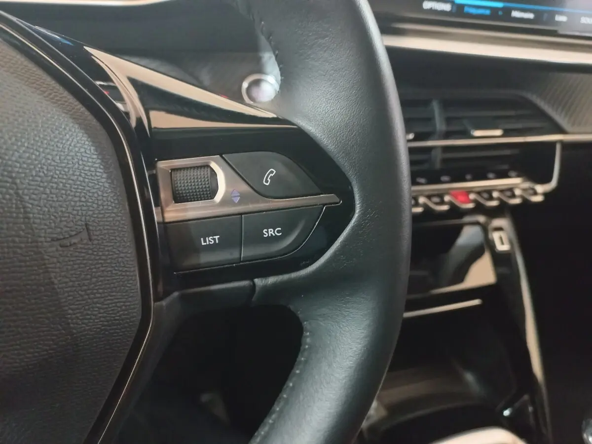 Gros plan sur le volant cuir noir de la Peugeot 2008 2021 avec commandes audio et tableau de bord moderne.