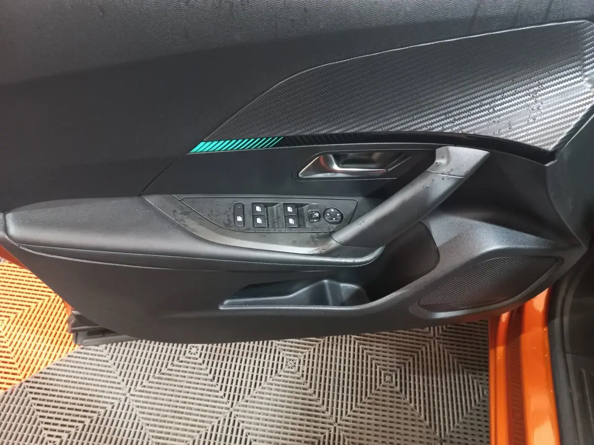 Gros plan sur la porte côté conducteur noire avec insert décoratif bleu d'une Peugeot 2008 orange 2021.