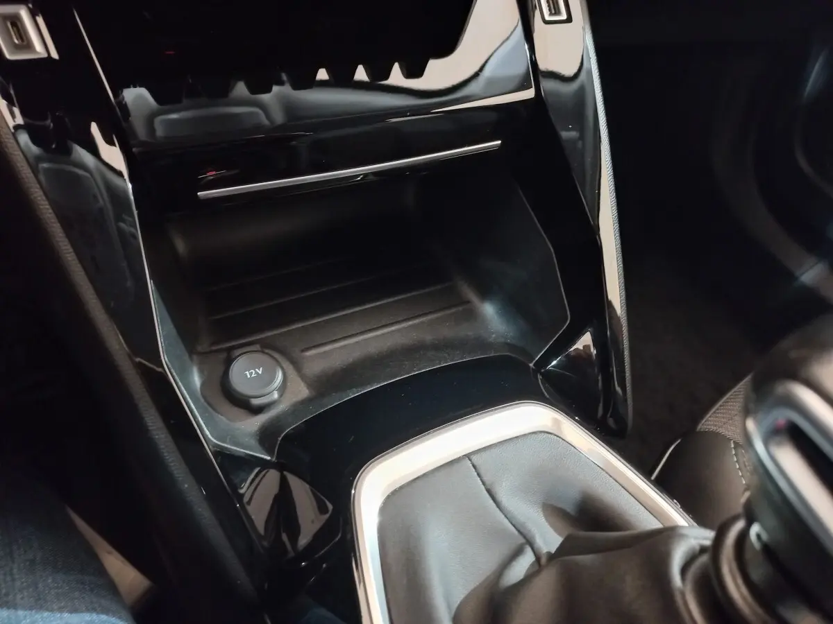 Gros plan sur la console centrale noire brillante avec prise 12V et levier de vitesse en cuir du Peugeot 2008 orange.