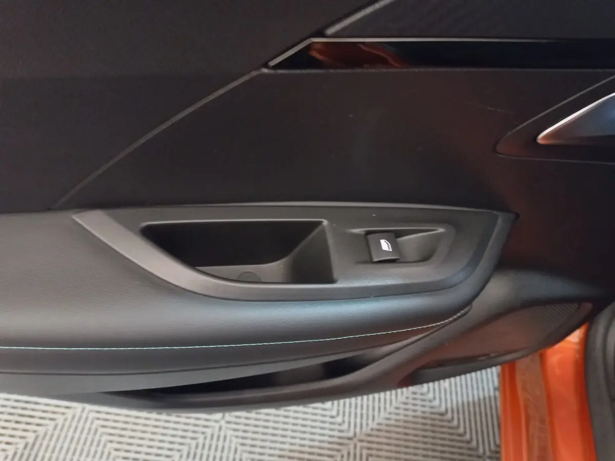 Gros plan sur la porte côté droit d'une Peugeot 2008 orange, montrant la commande de lève-vitre et le revêtement noir.
