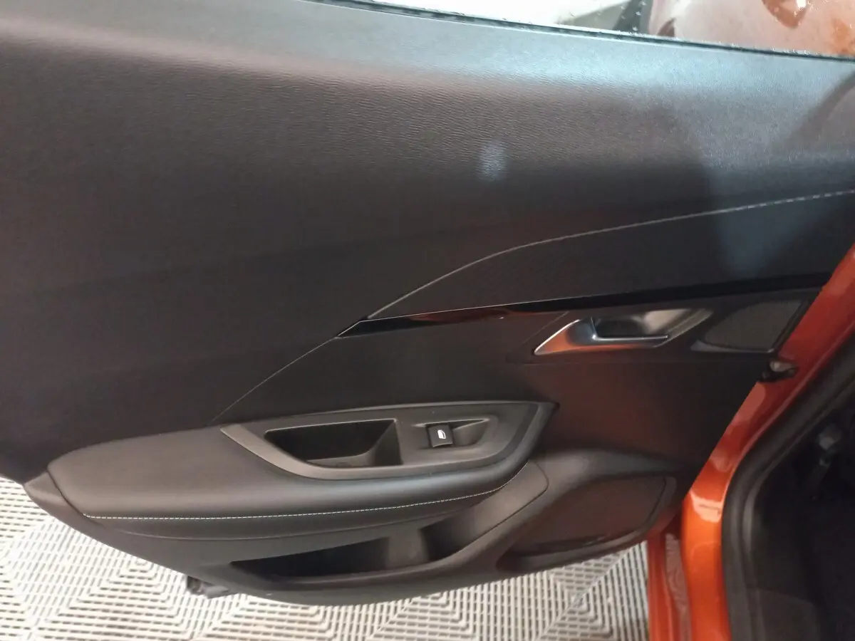 Intérieur de la porte côté gauche d'une Peugeot 2008 orange 2021, avec garniture noire et bouton de verrouillage.